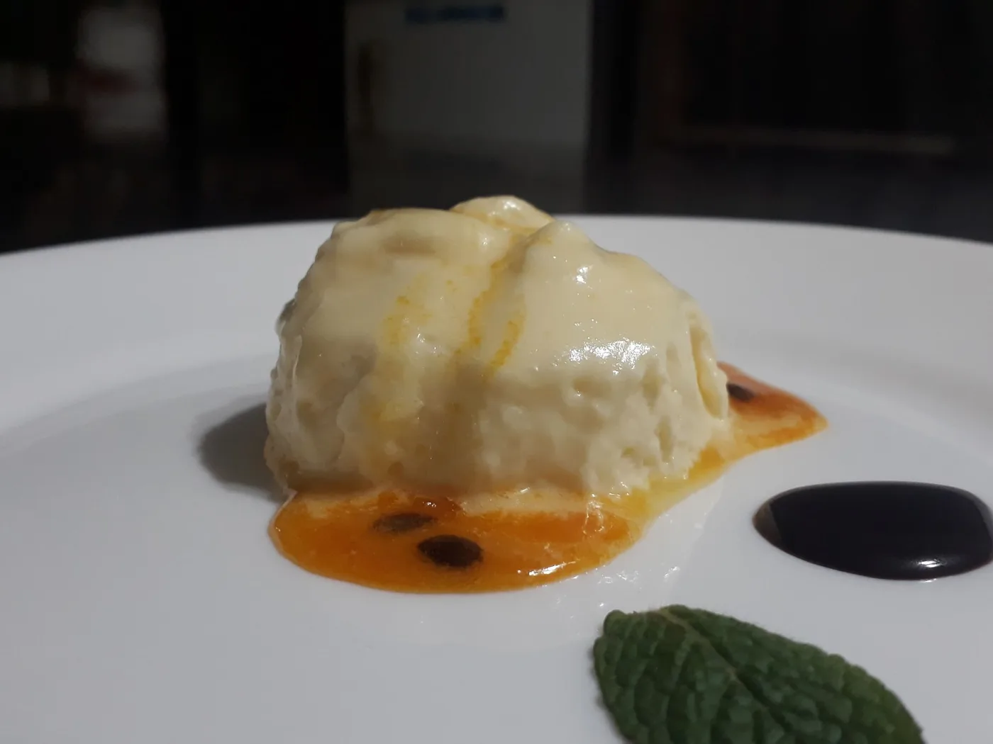 Mousse de maracuyá sobre salsa de la fruta, con hoja de menta y gota de chocolate