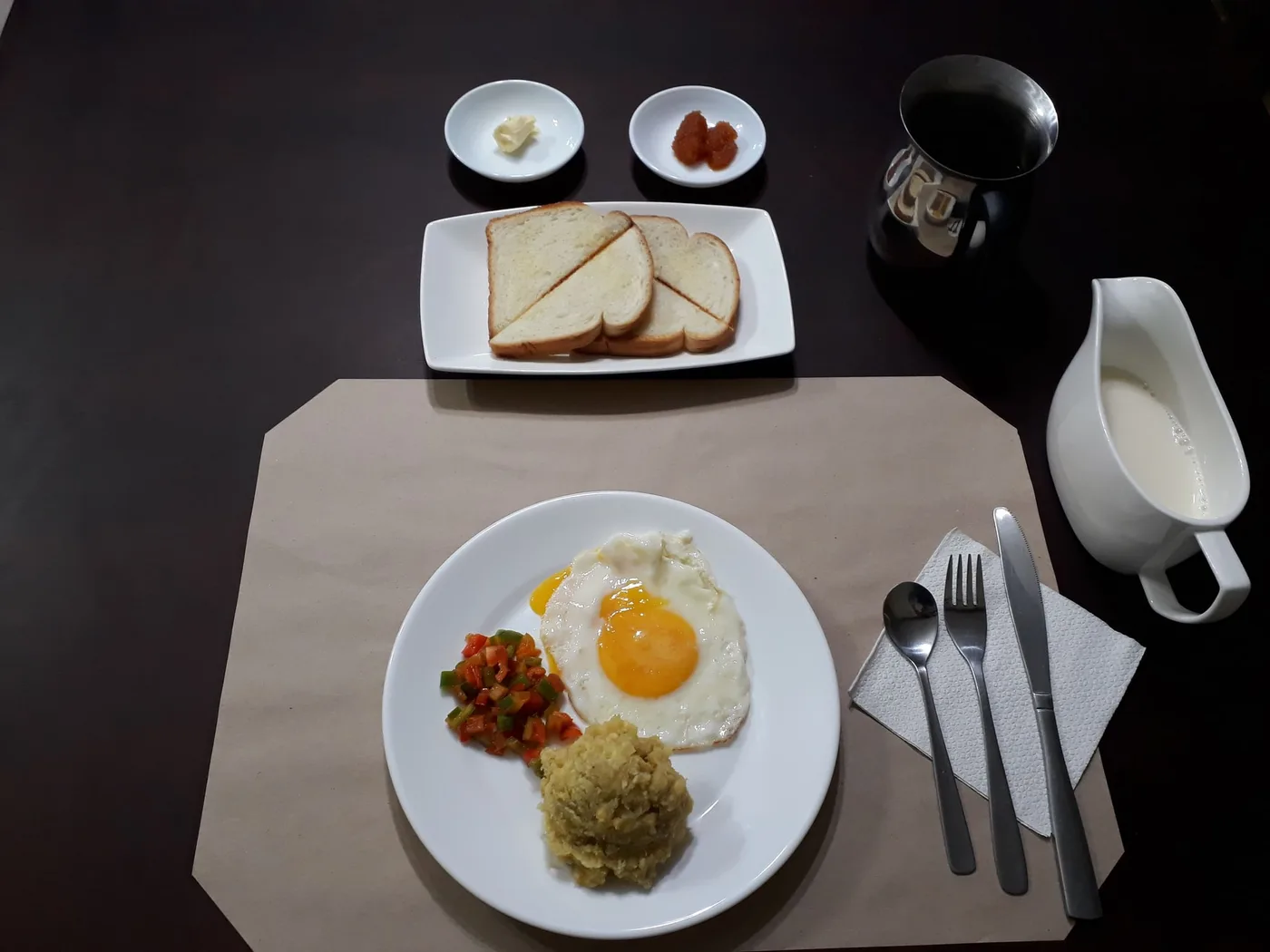 Desayuno servido: huevo frito, tostadas, mantequilla, mermelada y leche
